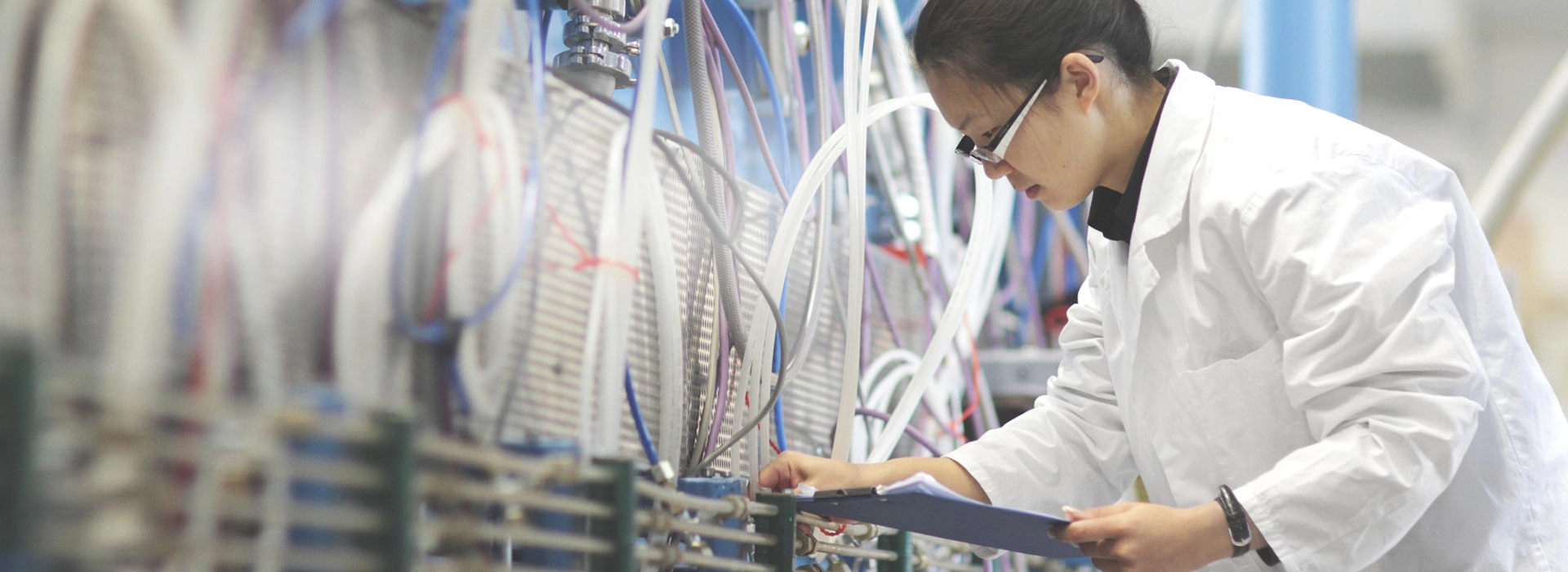 A woman checking the wires of a machine with a lab coat.